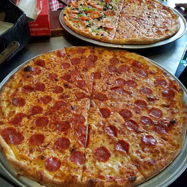 Two large pizzas on metal trays, one pepperoni and one with various toppings.