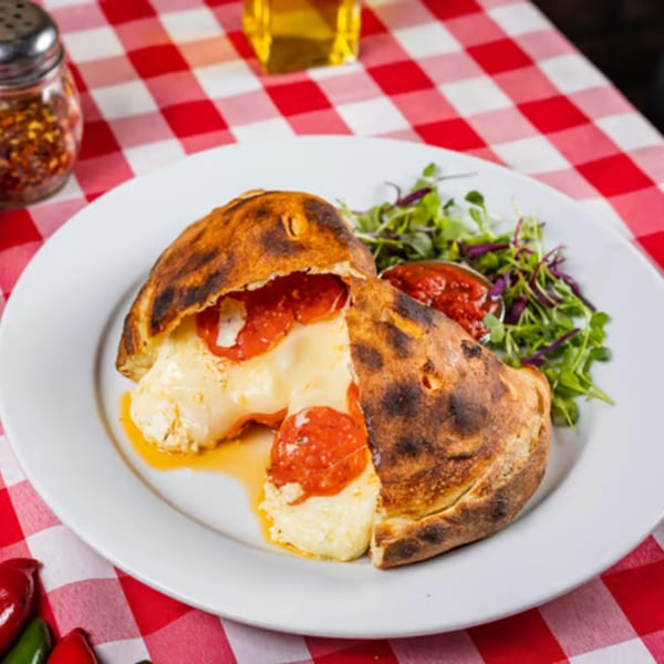 Enzo's Pizzeria calzone, cut open to reveal melted cheese and pepperoni, served with a side salad.