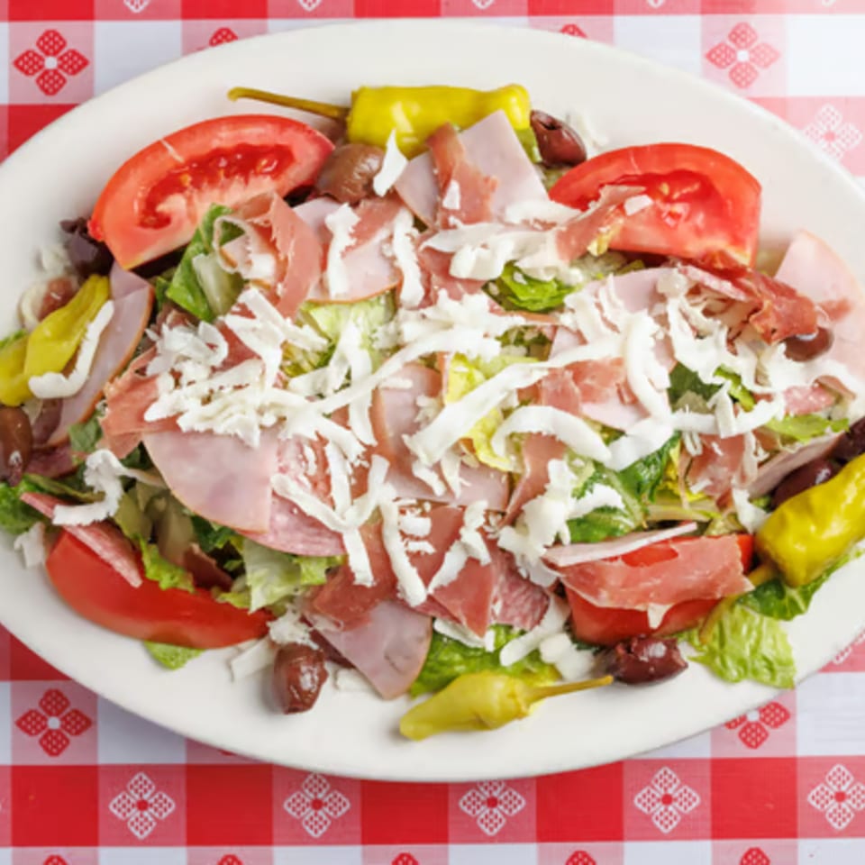 Enzo's Pizzeria antipasto salad with lettuce, tomatoes, olives, ham, salami, and shredded cheese.