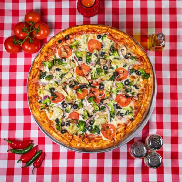Enzo's Pizzeria's large veggie pizza with tomatoes, olives, broccoli, and artichokes on a red checkered tablecloth.
