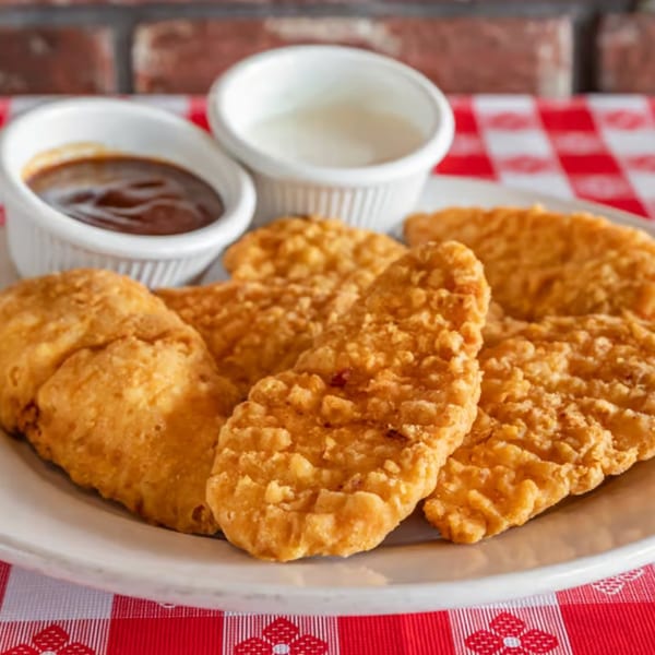 Crispy chicken tenders with barbecue and ranch dipping sauces on a red and white checkered tablecloth.