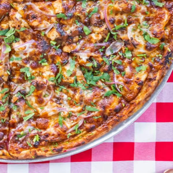 Enzo's Pizzeria's BBQ chicken pizza with red onions and cilantro on a red and white checkered tablecloth.