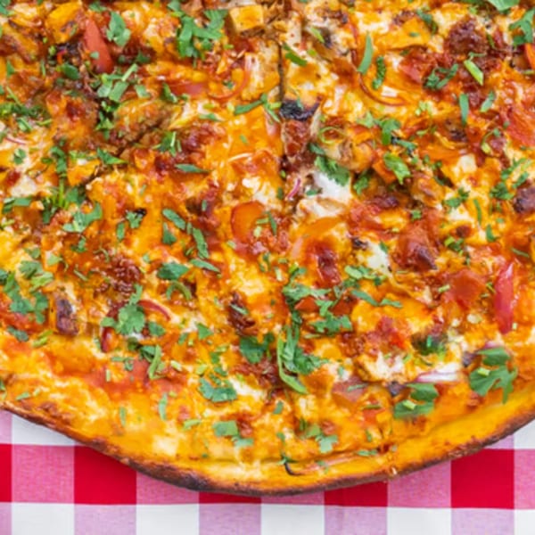 Enzo's Pizzeria's chicken tikka pizza with cilantro on a red and white checkered tablecloth.
