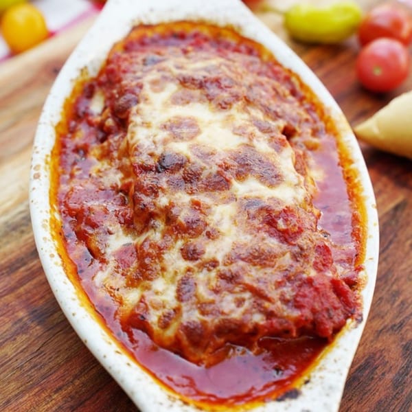 Baked lasagna with melted cheese and rich red sauce in a white dish on a wooden table.
