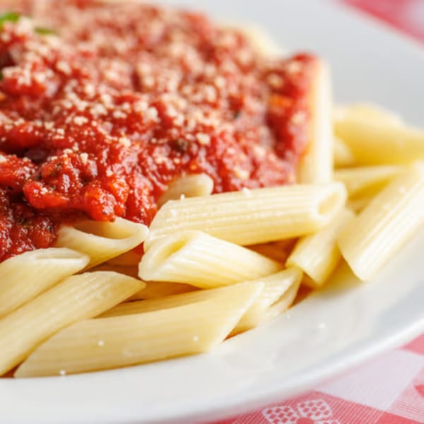Penne pasta with rich red marinara sauce and grated cheese on a white plate.