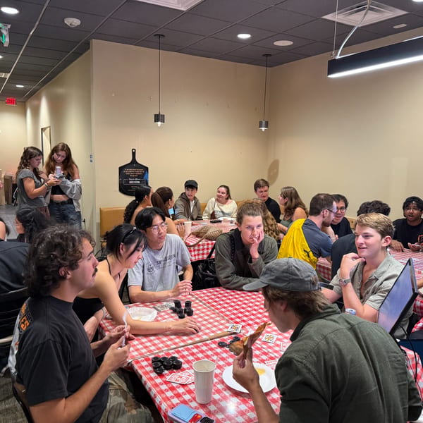 Customers gather at Enzo's Pizzeria, enjoying pizza and playing cards at tables with red and white checkered tablecloths.