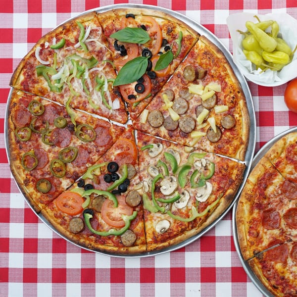 Two Enzo's Pizzeria pizzas on a red and white checkered tablecloth, one with various toppings.