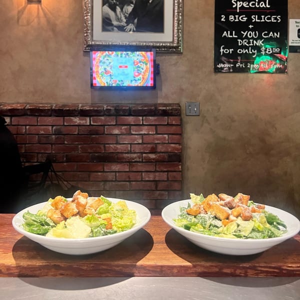 Two Caesar salads with croutons and parmesan cheese on a wooden counter at Enzo's Pizzeria.