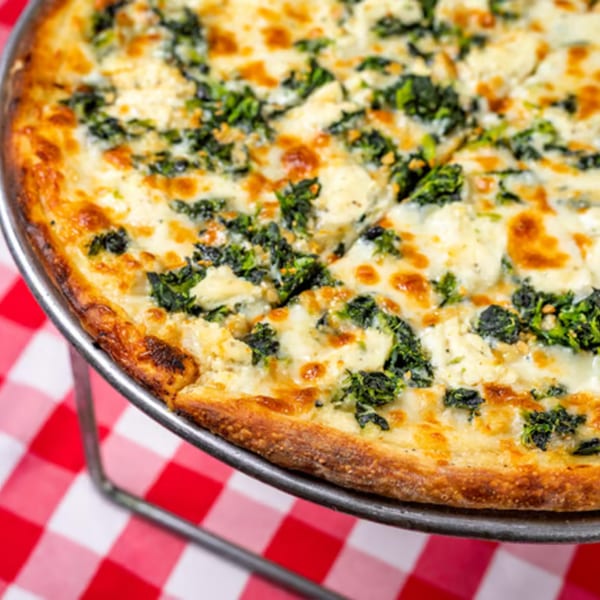 Enzo's Pizzeria white pizza with spinach and ricotta cheese on a red and white checkered tablecloth.