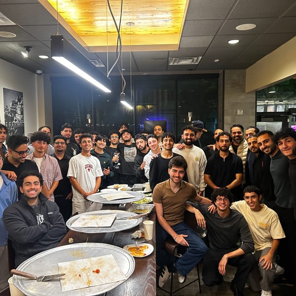 A large group of men smiling and posing around tables with empty pizza trays at Enzo's Pizzeria.