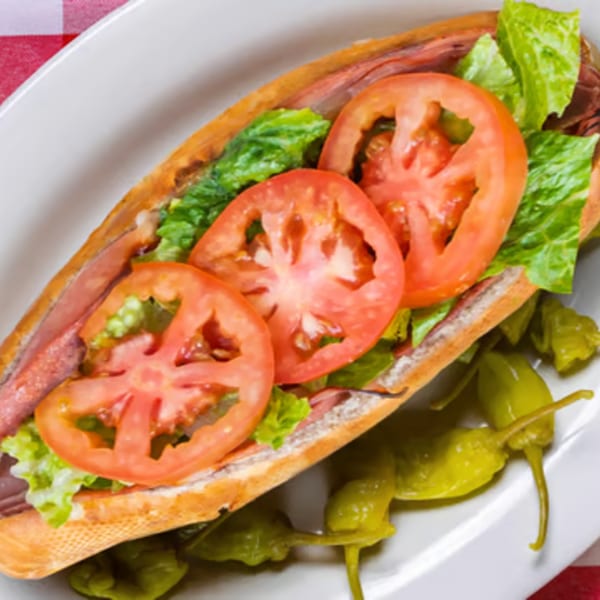 Enzo's Pizzeria sub sandwich with sliced tomatoes, lettuce, and peppers on a white plate.