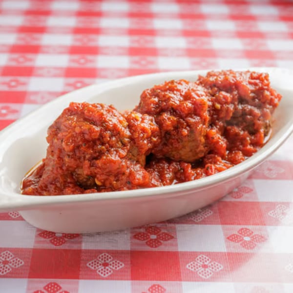 Three meatballs covered in rich red tomato sauce, served in a white dish on a red and white checkered tablecloth.